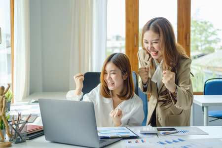 startup, successful, portrait of two young Asian women working on laptop computers, delighted with sales targets planned marketing.の写真素材