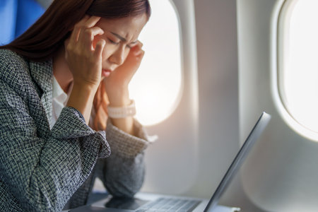 portrait of a successful Asian businesswoman or entrepreneur in a formal suit on an airplane seated in Business Class shows a thoughtful and stressed face with using laptop during the flight.の写真素材