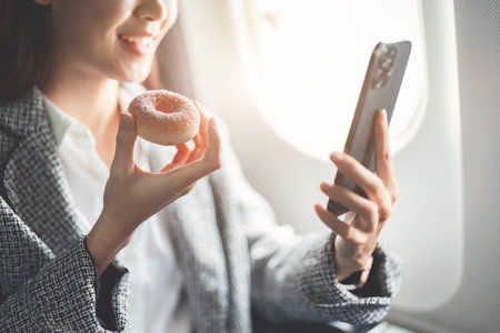 portrait of A successful asian businesswoman or female entrepreneur in formal suit in a plane sits in a business class seat and eating and using smartphone during flight.の写真素材