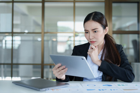 Portrait of a thoughtful Asian businesswoman looking at financial statements and making marketing plans using a tablet computer on her desk.の写真素材