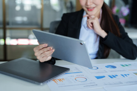 Portrait of a thoughtful Asian businesswoman looking at financial statements and making marketing plans using a tablet computer on her desk.の写真素材
