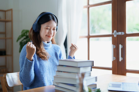 Portrait of young beautiful Asian woman showing smiling face during early morning online class with books, headphones and computer as study materials at home.の写真素材