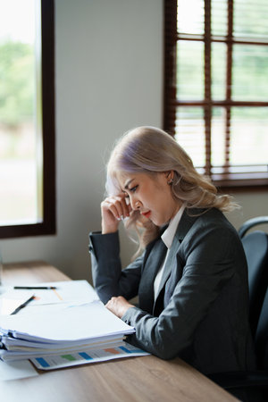 Portrait of a young Asian woman showing a serious face as she using financial documents and computer laptop on her desk in the early morning hours.の写真素材