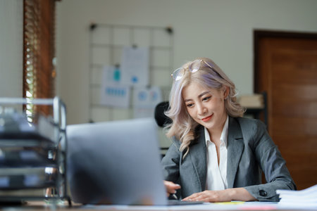 Portrait of a thoughtful Asian businesswoman looking at financial statements and making marketing plans using a computer on her desk.の写真素材