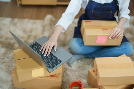 Starting small business entrepreneur of independent Asian woman smiling using computer laptop with cheerful success of online marketing package box items and SME delivery concept.の写真素材