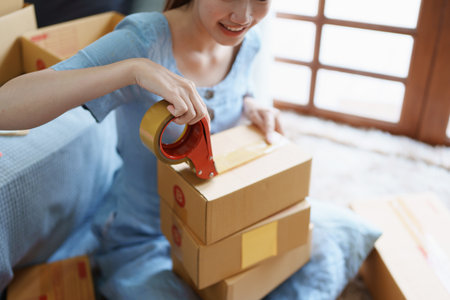 Starting small business entrepreneur of independent Asian female online seller packing products to...