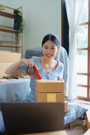 Starting small business entrepreneur of independent Asian female online seller packing products to...