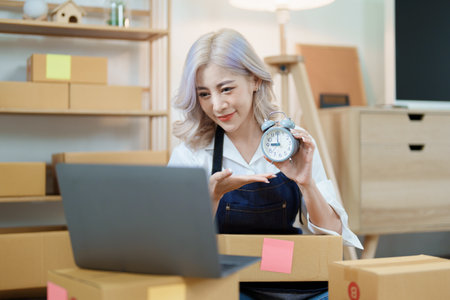 Starting small business entrepreneur of independent Asian woman smiling using computer laptop with cheerful success of online marketing package box items and SME delivery concept.の写真素材