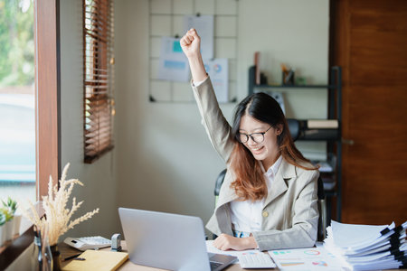 Portrait of a woman business owner showing a happy smiling face as he has successfully invested her business using computers and financial budget documents at work.の写真素材