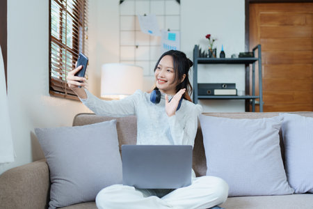 Portrait of a beautiful Asian teenage girl using her phone and computer for video conferencing...