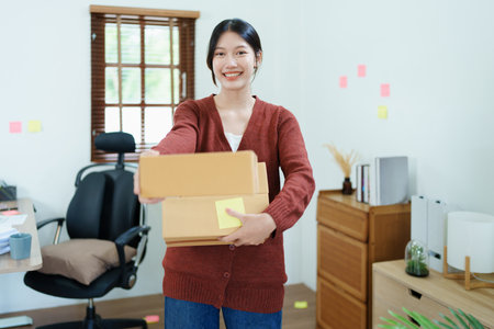 Starting small business entrepreneur of independent Asian woman smiling using computer laptop with cheerful success of online marketing package box items and SME delivery concept.の写真素材