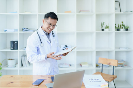 Portrait of a doctor looking at a patients information before treating a disease with using document and computer in work.の写真素材