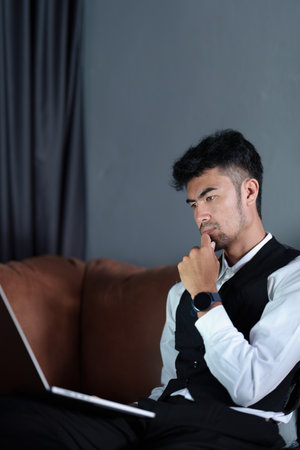 Portrait of a handsome, discreet Asian man sitting on the sofa using a computer.の写真素材