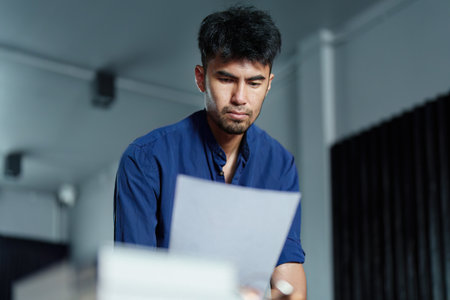 A portrait of a good-looking and discreet Asian man sitting at his desk with a thoughtful look on his computer.の写真素材