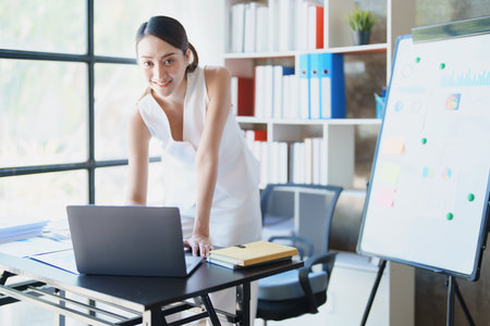 Portrait of a woman business owner showing a happy smiling face as he has successfully invested her business using computers and financial budget documents at work.の写真素材