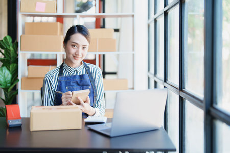 Starting small business entrepreneur of independent young Asian woman online seller is using computer and taking orders to pack products for delivery to customers. SME delivery concept.の写真素材