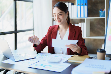 Portrait of a thoughtful Asian businesswoman looking at financial statements and making marketing plans using a computer on her desk.の写真素材