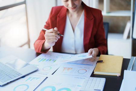Portrait of a thoughtful Asian businesswoman looking at financial statements and making marketing plans using a computer on her desk.の写真素材