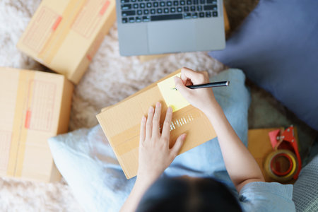 Starting small business entrepreneur of independent young Asian woman online seller is using computer and taking orders to pack products for delivery to customers. SME delivery concept.の写真素材