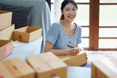 Starting small business entrepreneur of independent young Asian woman online seller is using computer and taking orders to pack products for delivery to customers. SME delivery concept.の写真素材