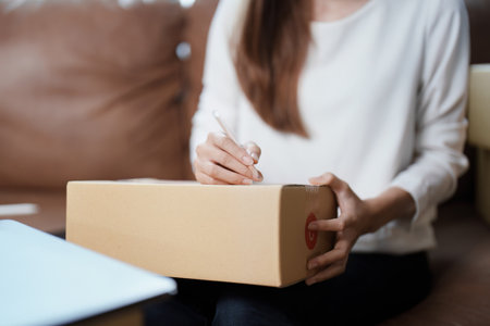 Starting small business entrepreneur of independent young Asian woman online seller is using computer and taking orders to pack products for delivery to customers. SME delivery concept.の写真素材