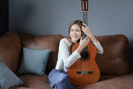 Portrait of young asian woman playing guitar on sofa relaxing stress on vacation.