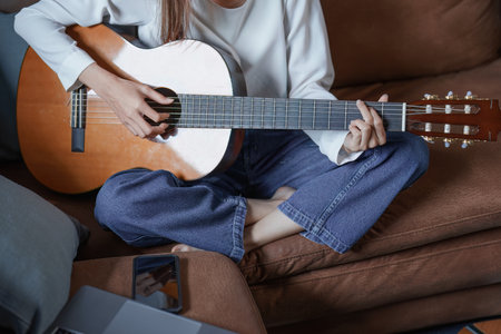Portrait of young asian woman playing guitar on sofa relaxing stress on vacation.の写真素材