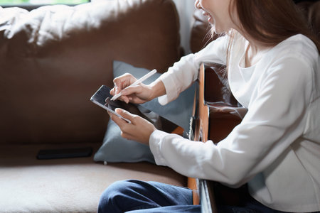 Portrait of young asian woman playing guitar on sofa relaxing stress on vacation.の写真素材