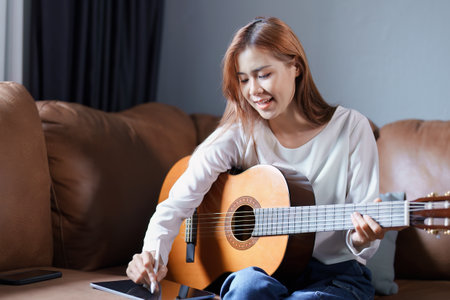 Portrait of young asian woman playing guitar on sofa relaxing stress on vacation.の写真素材