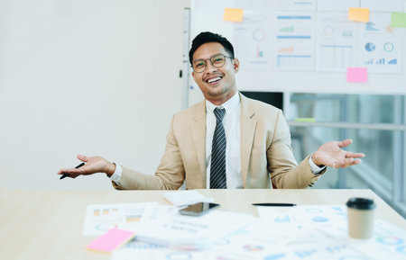 Portrait of a male business owner showing a happy smiling face as he has successfully invested his business using computers and financial budget documents at work.の写真素材