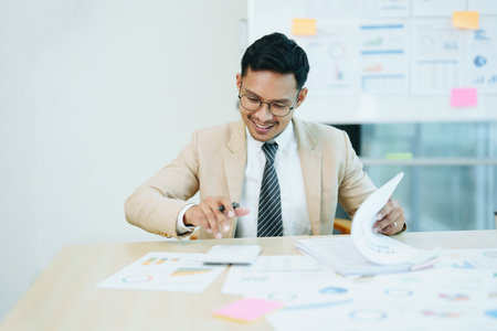 Portrait of an Asian male accountant working on a desk calculating taxes from annual financial documents using a calculator at work.の写真素材