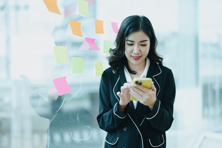 A portrait of an Asian business owner showing a smiling and happy face using her phone standing by a...