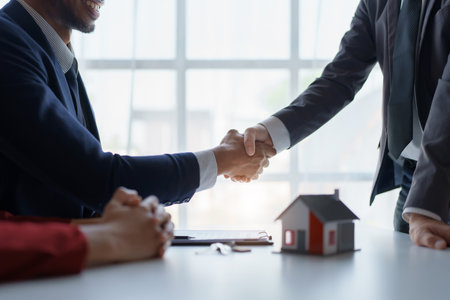 Asian real estate agent shaking hands handing over house and keys to his clients house after client sign contractの写真素材