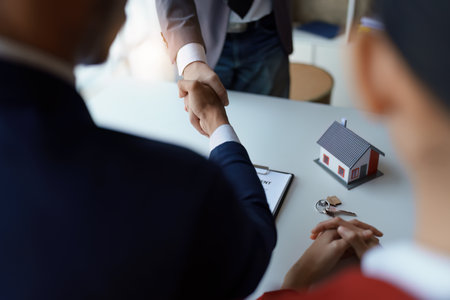 Asian real estate agent shaking hands handing over house and keys to his clients house after client sign contractの写真素材