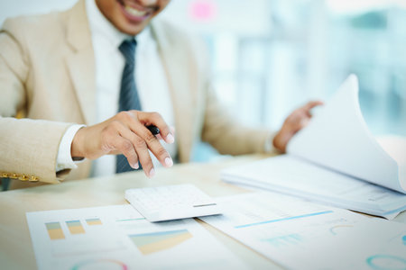 Portrait of an Asian male accountant working on a desk calculating taxes from annual financial documents using a calculator at work.の写真素材