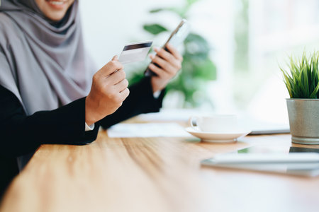 Beautiful Muslim woman shopping online using her phone and credit card.の写真素材