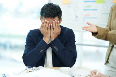 An image of an Asian male employee looking worried and sad about being scolded by his boss for failing to meet sales targets, concept of disappointment and failure in his career.の写真素材