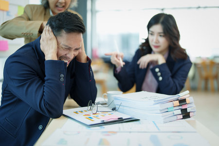 An image of an Asian male employee looking worried and sad about being scolded by his boss for failing to meet sales targets, concept of disappointment and failure in his career.の写真素材