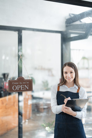 Starting and opening a small business, a young Asian woman showing a smiling face in an apron standing in front of a coffee shop bar counter. Business Owner, Restaurant, Barista, Cafe, Online SME.の写真素材