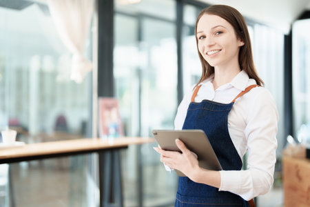 Starting and opening a small business, a young Asian woman showing a smiling face in an apron standing in front of a coffee shop bar counter. Business Owner, Restaurant, Barista, Cafe, Online SME.の写真素材