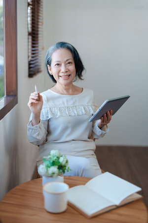 Portrait of an elderly Asian woman in a modern pose working on a tablet computerの写真素材