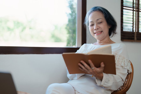 Portrait of an elderly Asian woman in a modern pose holding a memory notebook and operating a computerの写真素材