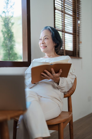 Portrait of an elderly Asian woman in a modern pose holding a memory notebook and operating a computerの写真素材
