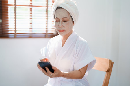Portrait of elderly woman doing face spa treatment and using mobile phoneの写真素材