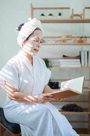 Portrait of elderly woman doing face spa treatment and using notebookの写真素材