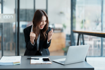 Portrait of a woman business owner showing a happy smiling face as he has successfully invested her business using computers and financial budget documents at work.の写真素材