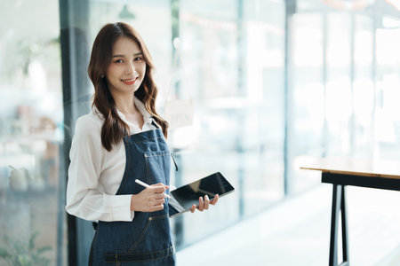 open a small business Portrait of happy Asian woman in apron holding tablet in front of cafeの写真素材