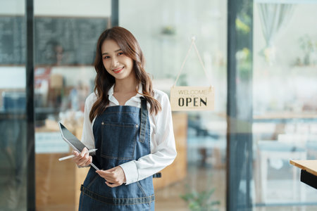 open a small business Portrait of happy Asian woman in apron holding tablet in front of cafe