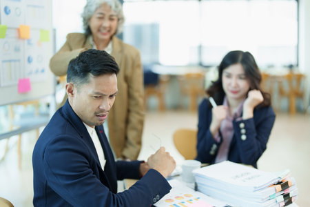 An image of an Asian male employee looking worried and sad about being scolded by his boss for failing to meet sales targets, concept of disappointment and failure in his career.の写真素材