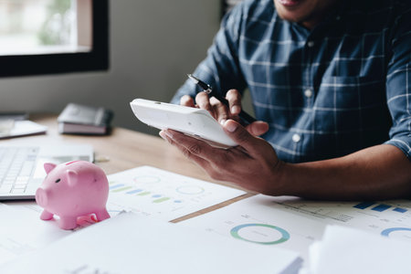 Portrait of an Asian businessman using a calculator to calculate his savings from SME operations, with a pink piggy bank as keep money concept.の写真素材